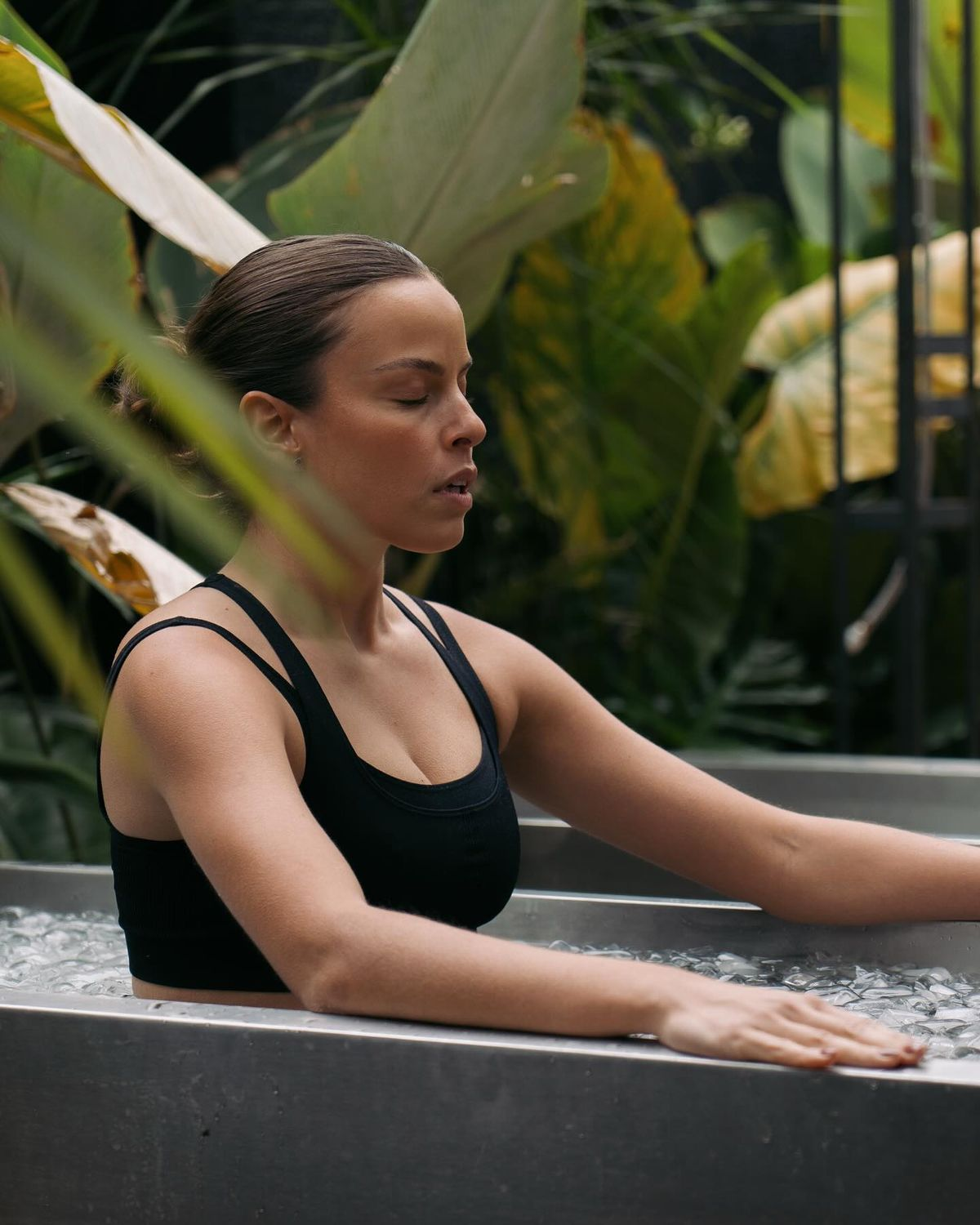 Mujer sumergida en cold plunge rodeada de vegetación