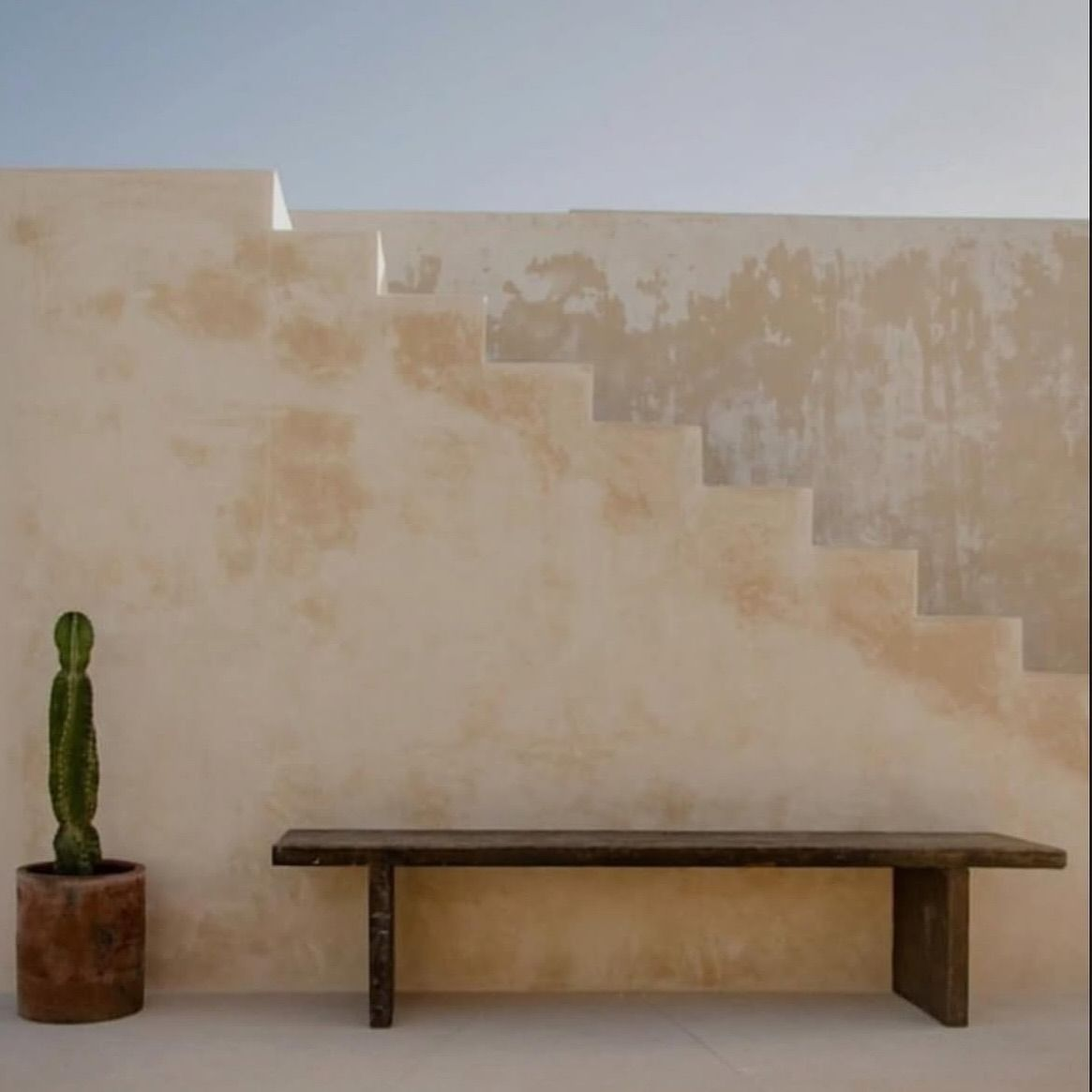 Muro de chukum con banca de madera y cactus en maceta de barro