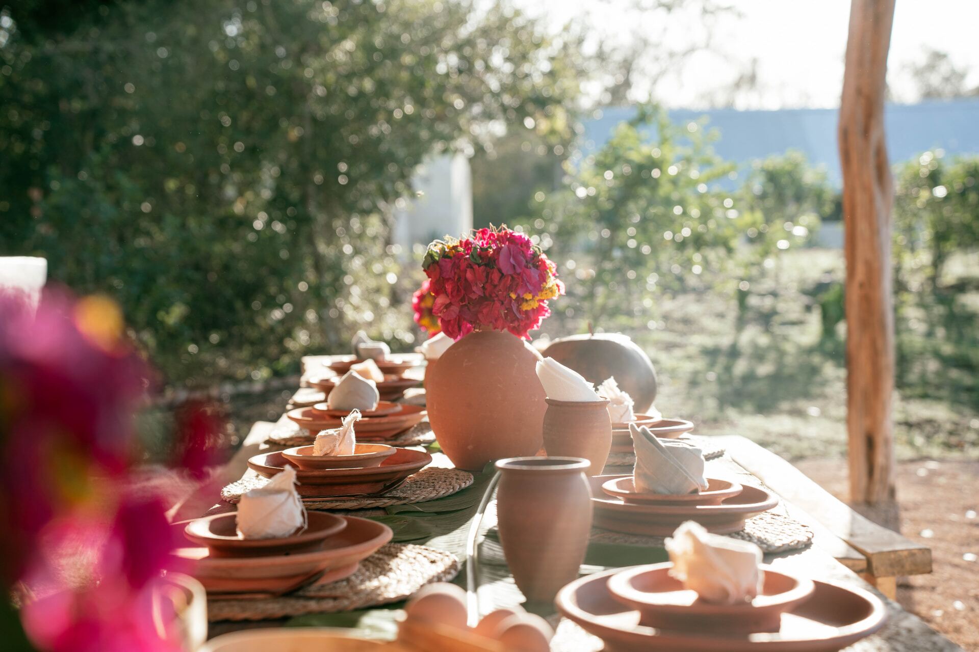 Mesa larga servida con vajilla de barro y flores del jardín