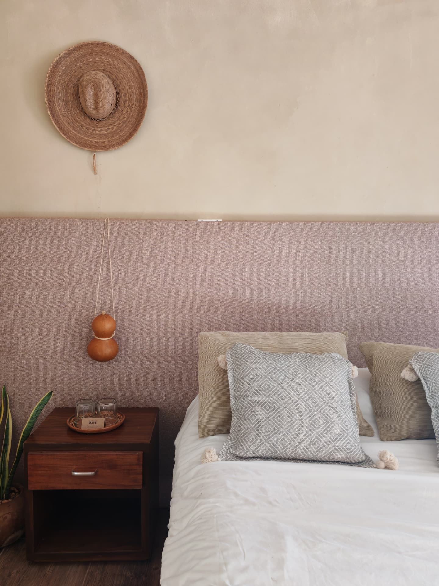 Recámara con cabecera textil, sombrero de palma y buró de madera