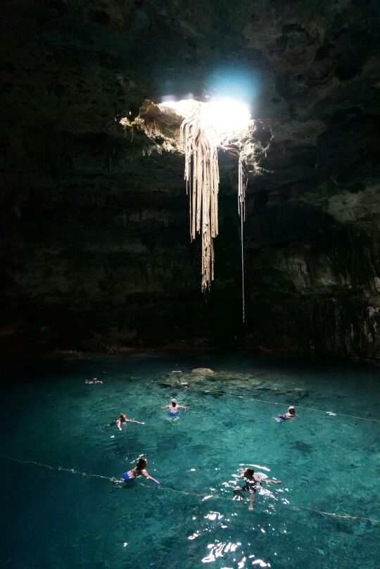 Cenote abierto con un haz de luz y raíces cayendo sobre el agua turquesa