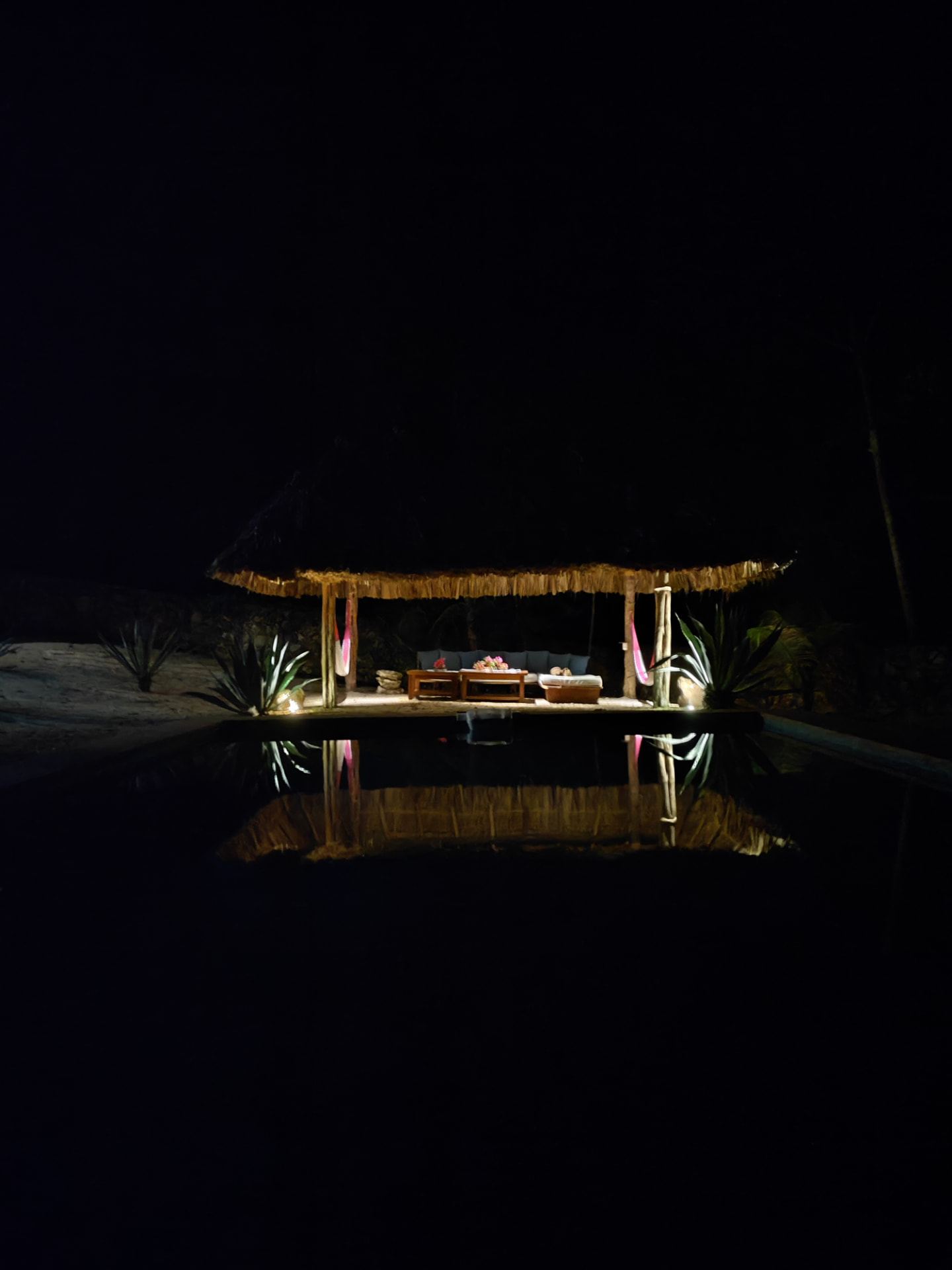 Palapa iluminada reflejada en el agua por la noche