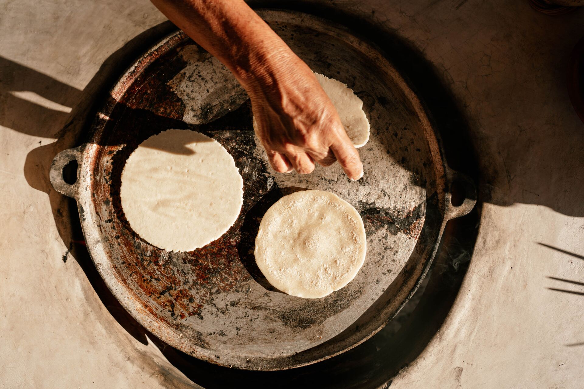 Manos colocando tortillas sobre un comal de barro
